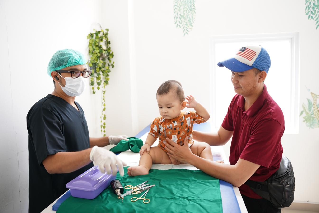 Dokter SunatBoss menyiapkan alat sunat sambil menenangkan pasien bayi